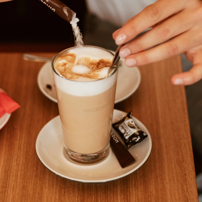 Ein Caffe Latte auf einem Holztisch mit einer J. Hornig Zucker-Packung.