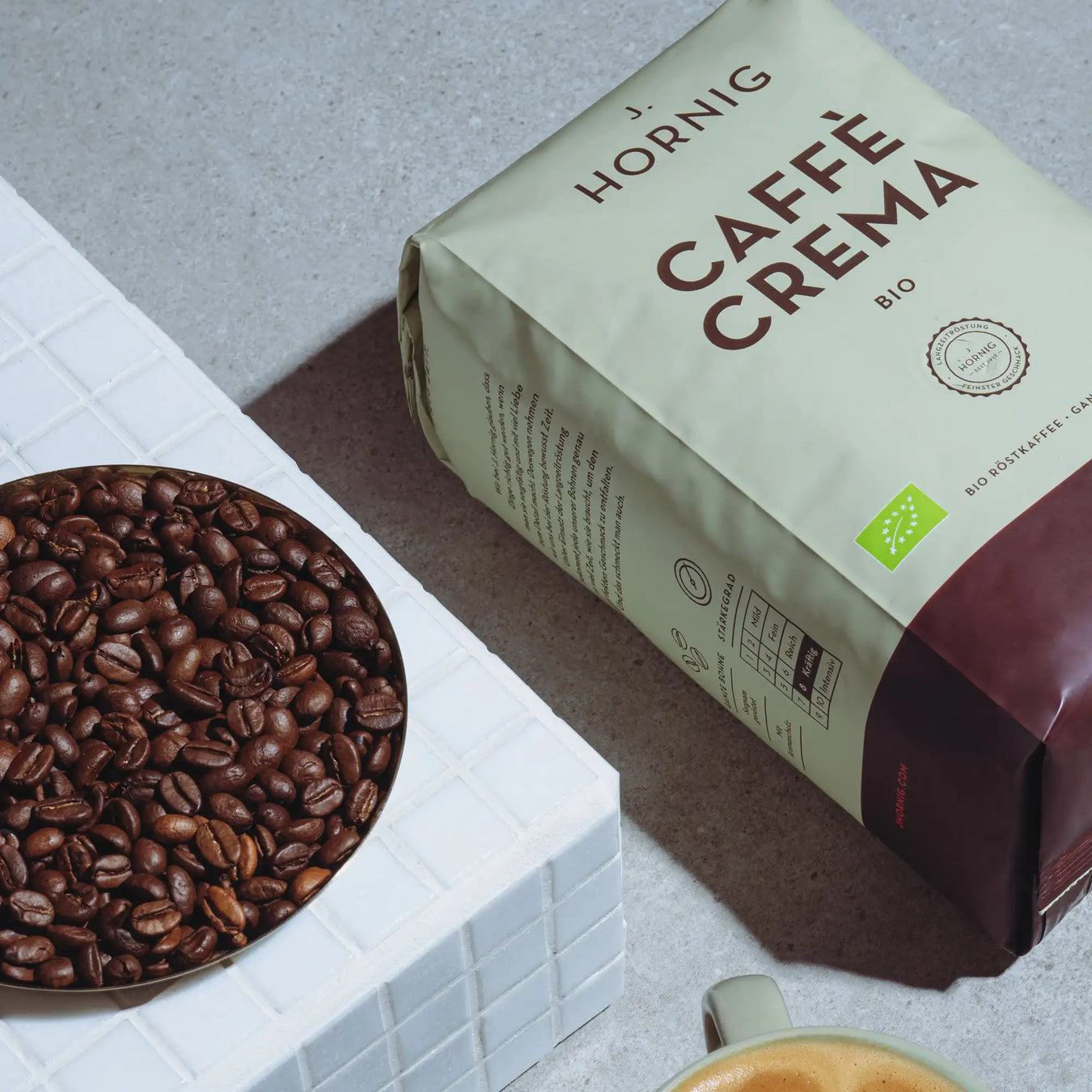 Eine Packung J. Hornig Caffe Crema Bio Kaffee liegend mit einer Schale Kaffeebohnen