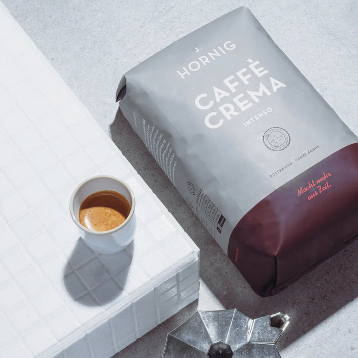 Eine Packung J. Hornig Caffe Crema Intenso liegend mit einem Espresso auf hellem Untergrund