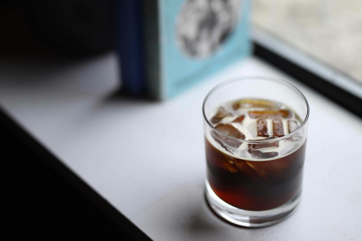 Eine Cold Brew Kaffee in einem Glas mit Eiswürfel auf einer Fensterbank.