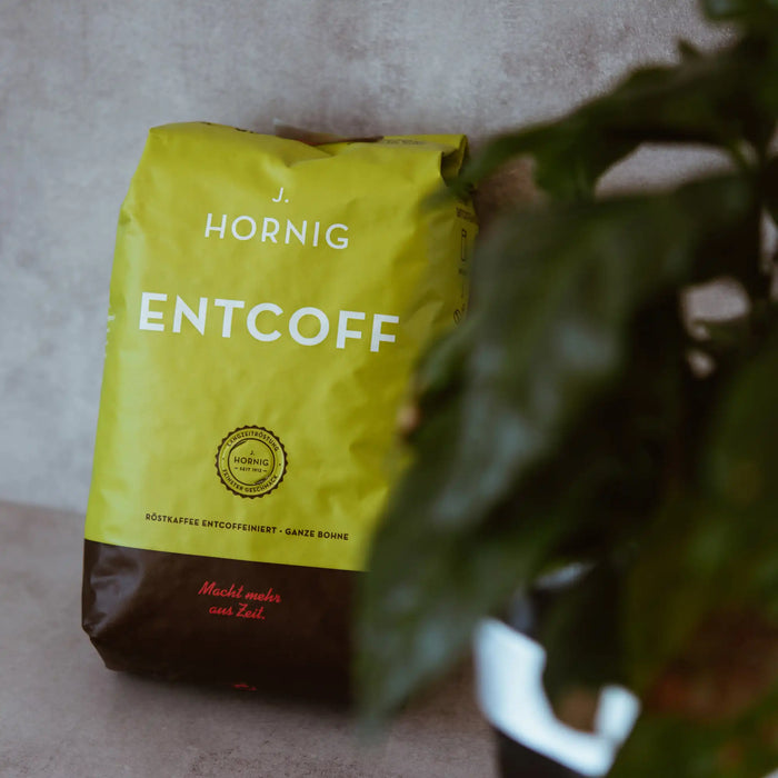 Eine Packung J. Hornig Entcoff Kaffee Ganze Bohne an einer Wand angelehnt mit einer Zimmerpflanze im Vordergrund
