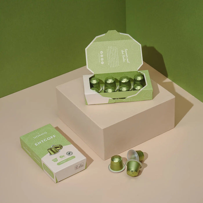 Eine offene Packung J. Hornig Entcoff Kapseln und eine geschlossene Packung J. Hornig Entcoff Kapseln auf einem hellen Untergrund mit grünem Hintergrund