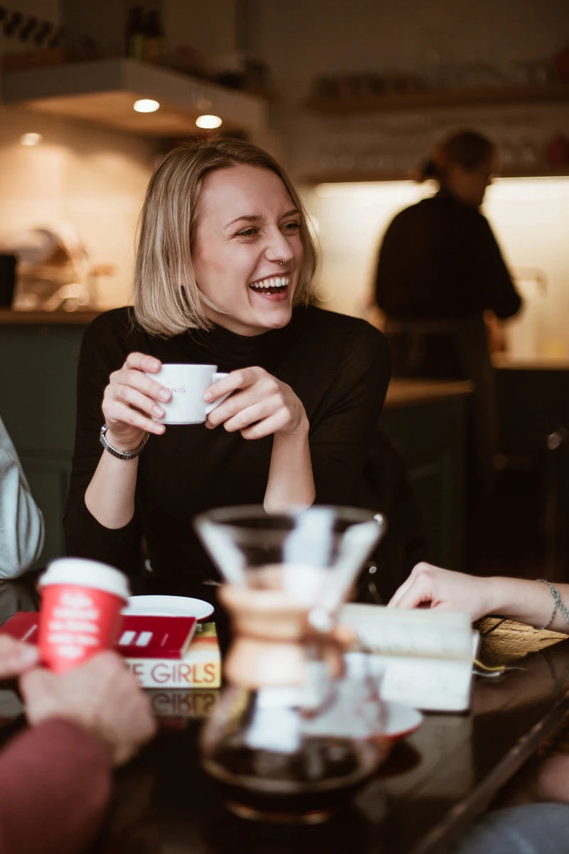 Eine lächelnde, junge Frau hält eine Tasse Kaffee in der Hand in einem Kaffeehaus