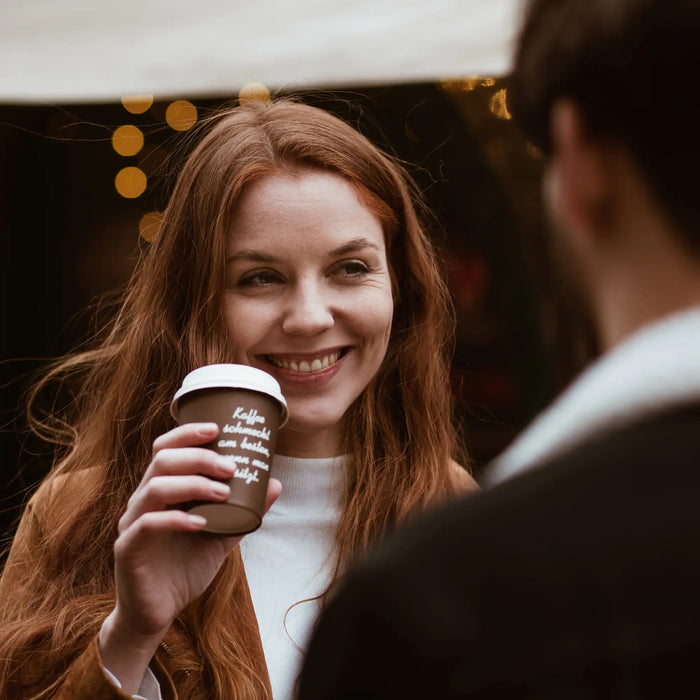Eine junge Frau trinkt aus einem J. Hornig Coffee-to-go Becher.