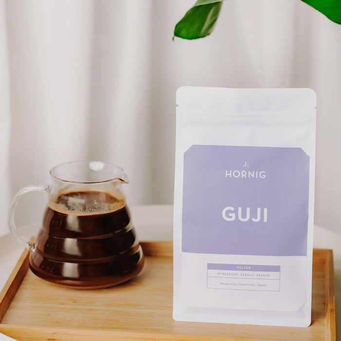 Packung J. Hornig Guji Spezialitätenkaffee auf einem Holztisch mit Espressokanne.