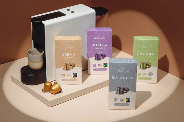 Vier Packungen J. Hornig Kaffeekapseln mit einer Kapselmaschine.