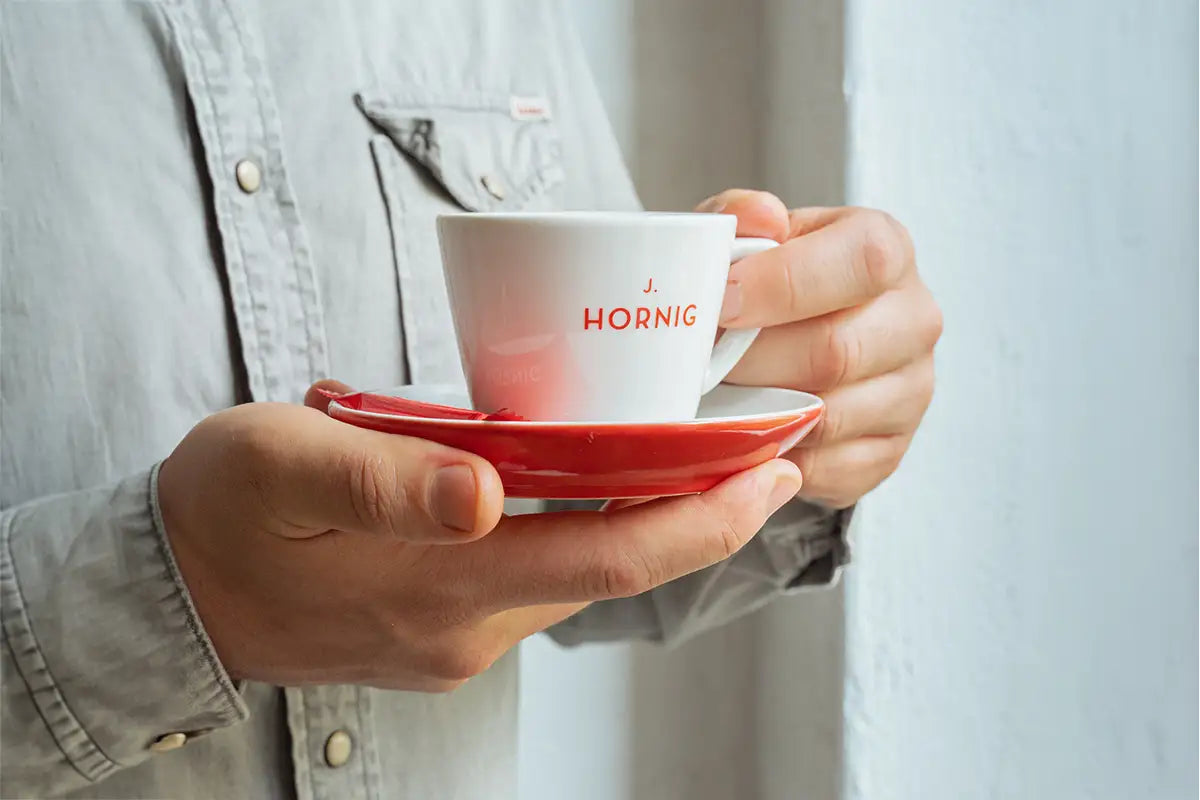 Eine Person hält eine Kaffeetasse von J. Hornig in den Händen