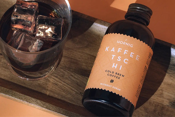 Eine Flasche J. Hornig Kaffeetschi Cold Brew auf einem Holzuntergrund mit einem vollem Glas