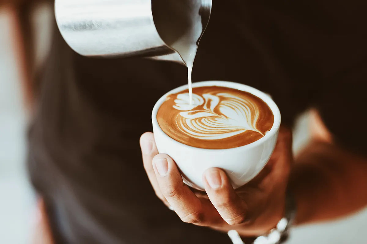 Eine Person macht Latte Art und hält einen Cappuccino in der Hand