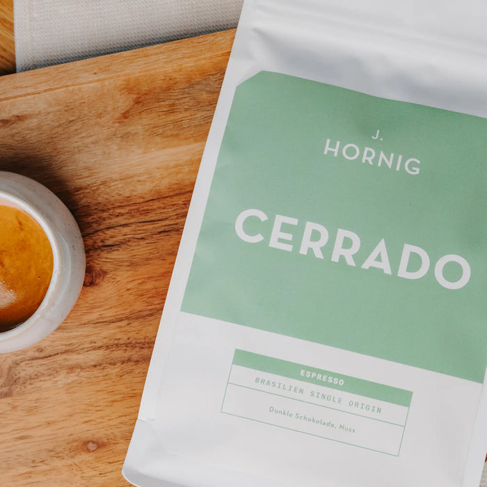 Eine Packung J. Hornig Spezialitätenkaffee Cerrado Espresso liegend auf einem Holztisch mit einer Espressotasse.