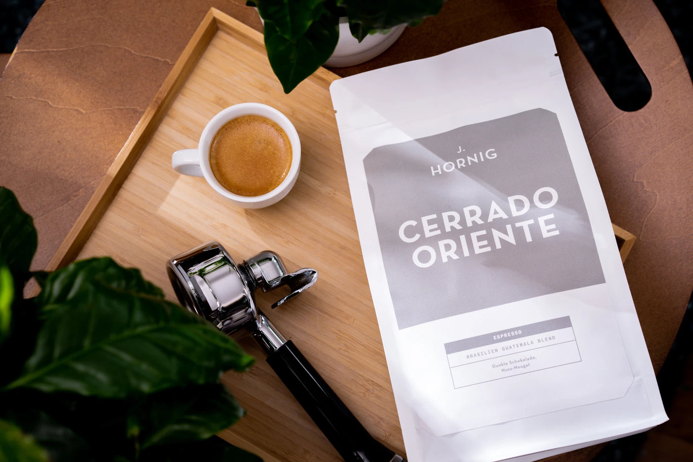 Eine Packung J. Hornig Spezialitätenkaffee Cerrado Oriente Espresso auf einem Holztablett mit einem Siebträger und einer Tasse Kaffee