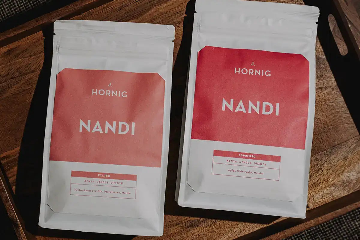 Eine Packung J. Hornig Spezialitätenkaffee Nandi Espresso und eine Packung J. Hornig Spezialitätenkaffee Nandi Filter auf einem Holztablett