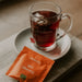 Eine Tasse Tee in einem J.Hornig Teeglas mit einer Einzelpackung Bio Orange Tee.