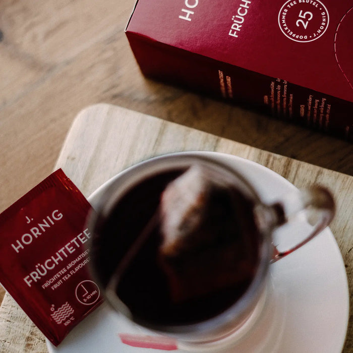 Eine Tasse Tee in einem J.Hornig Teeglas mit einer Einzelpackung Früchtetee..