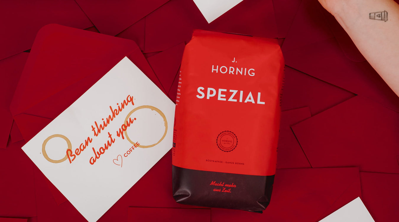 J. Hornig Spezial Kaffeepackung auf rotem Hintergrund, daneben eine weiße Karte mit handgeschriebenem Schriftzug, umgeben von roten Papierkuverts.