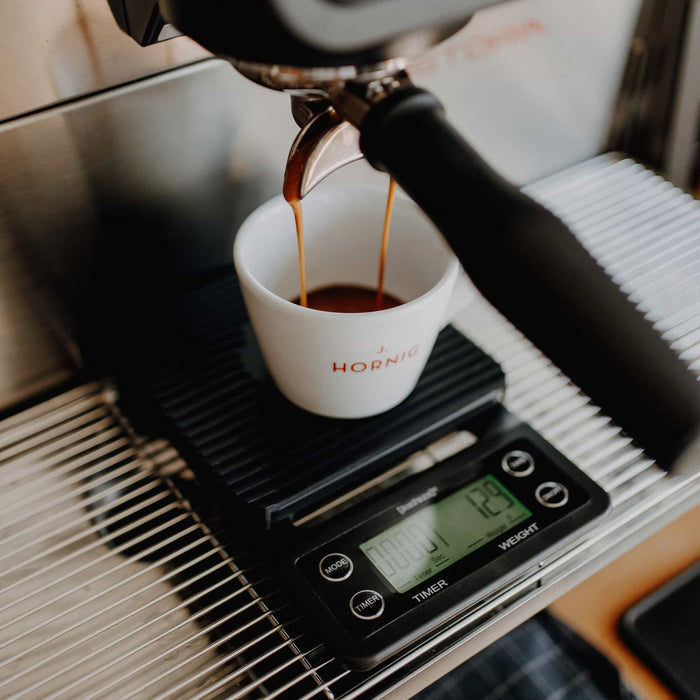 Frontalaufnahme eines Espressobezugs: Frischer Espresso läuft aus dem Siebträger in eine J. Hornig Tasse, die auf einer digitalen Waage steht.