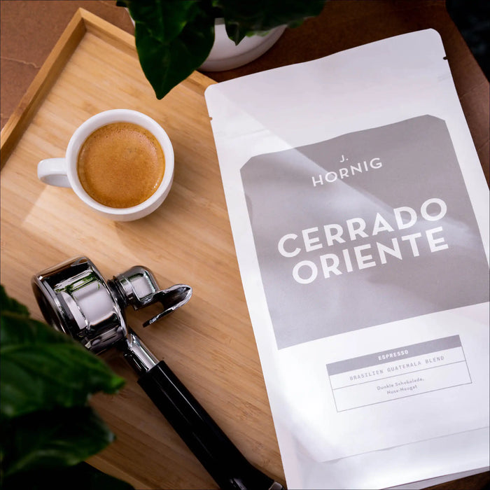 Eine Packung J. Hornig Spezialitätenkaffee Cerrado Oriente Espresso Brasilien Guatemala Blend liegend auf einem Holztablett mit einem Espresso und einem Siebträger