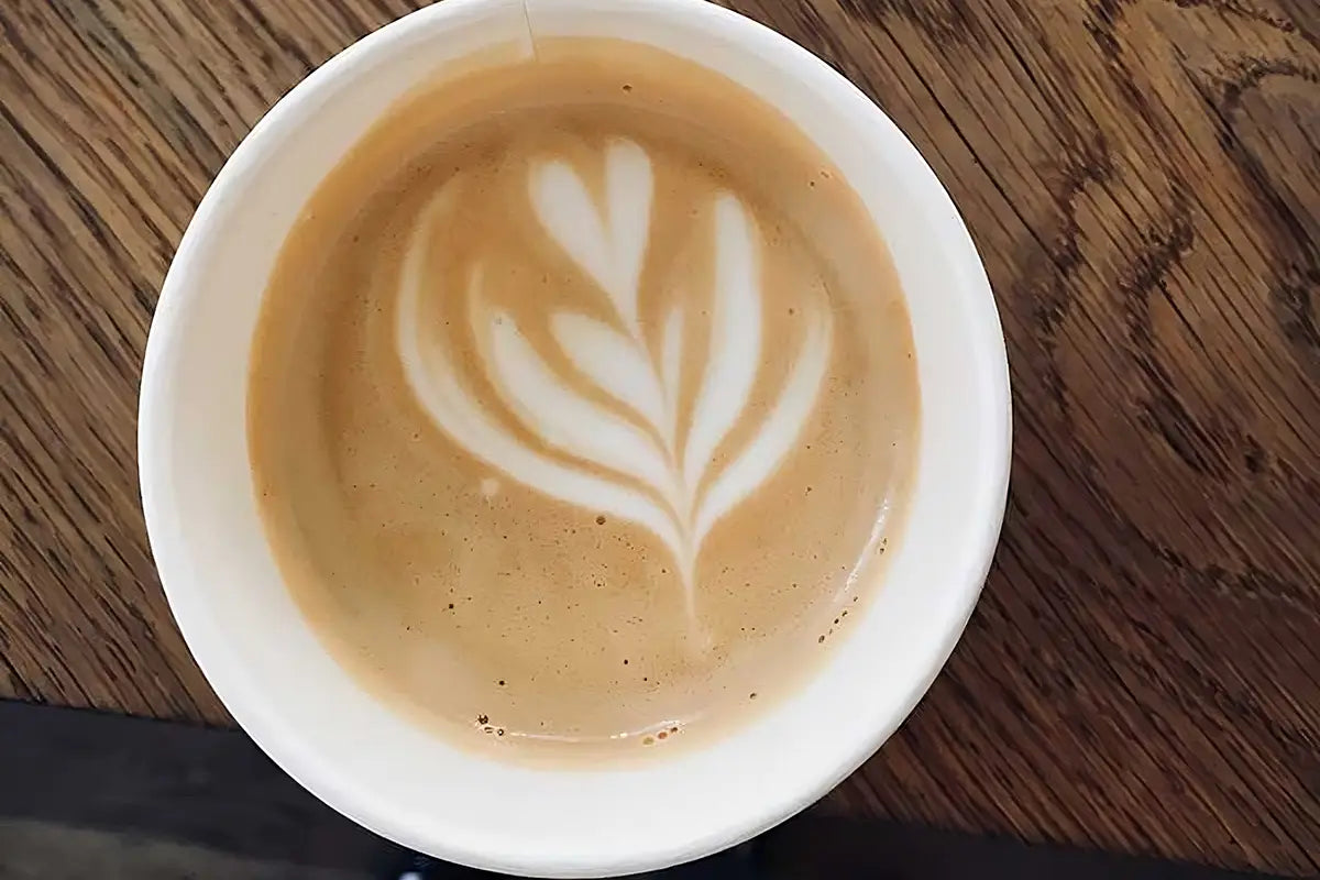 Ein Cappuccino mit Herz Latte Art steht auf einem Holztisch