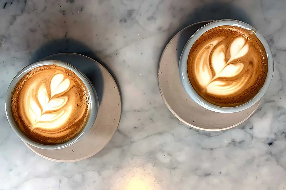 Auf einer marmorierten Platte stehen zwei Cappuccino Tassen mit Latte Art 