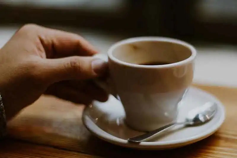 Eine Hand greift zu einer Espressotasse die auf einem Holzbrett steht 