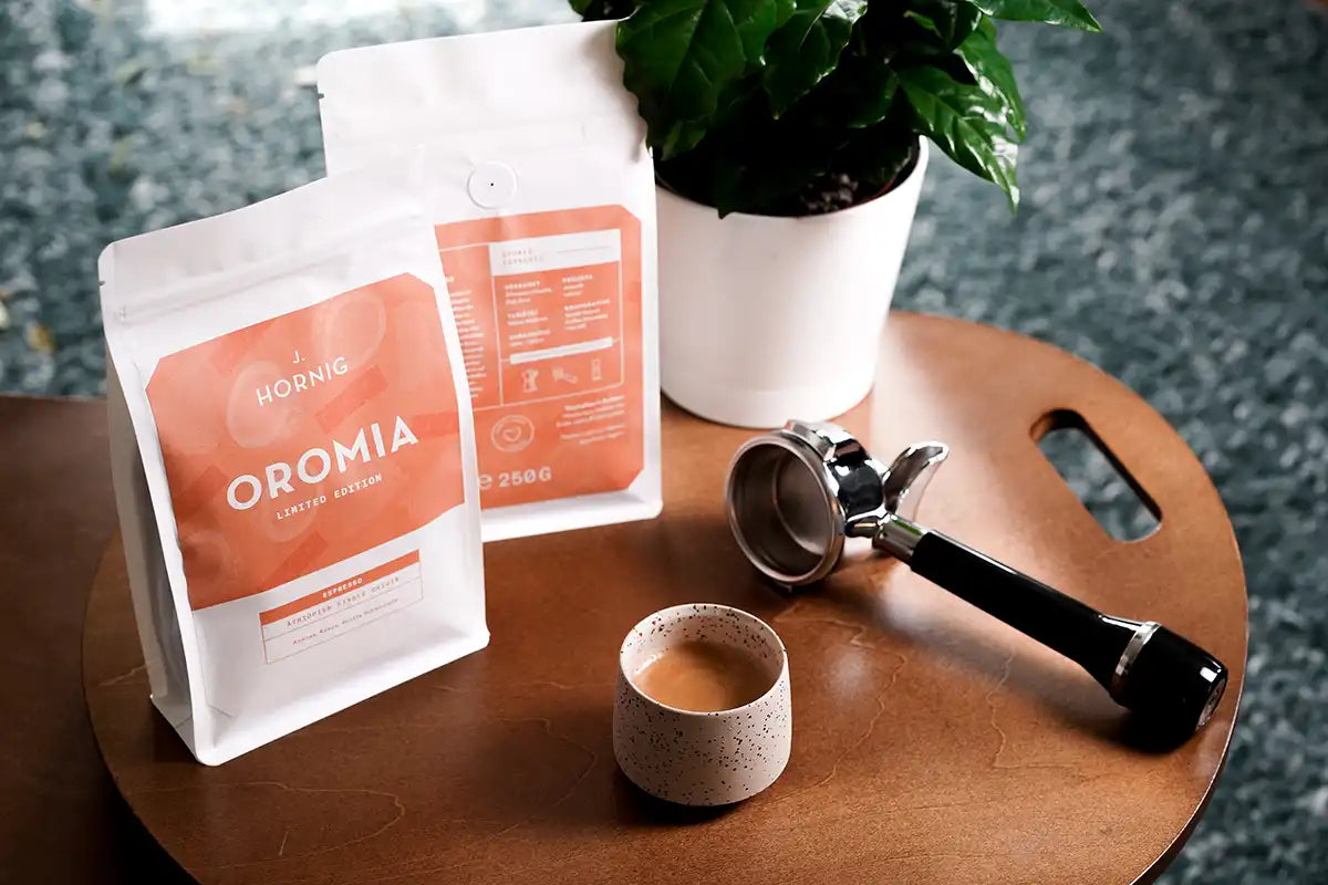 Die Vorder- und Rückseite des J. Hornig Oromia auf einem Tisch stehend mit einem Espresso und einem Siebträger