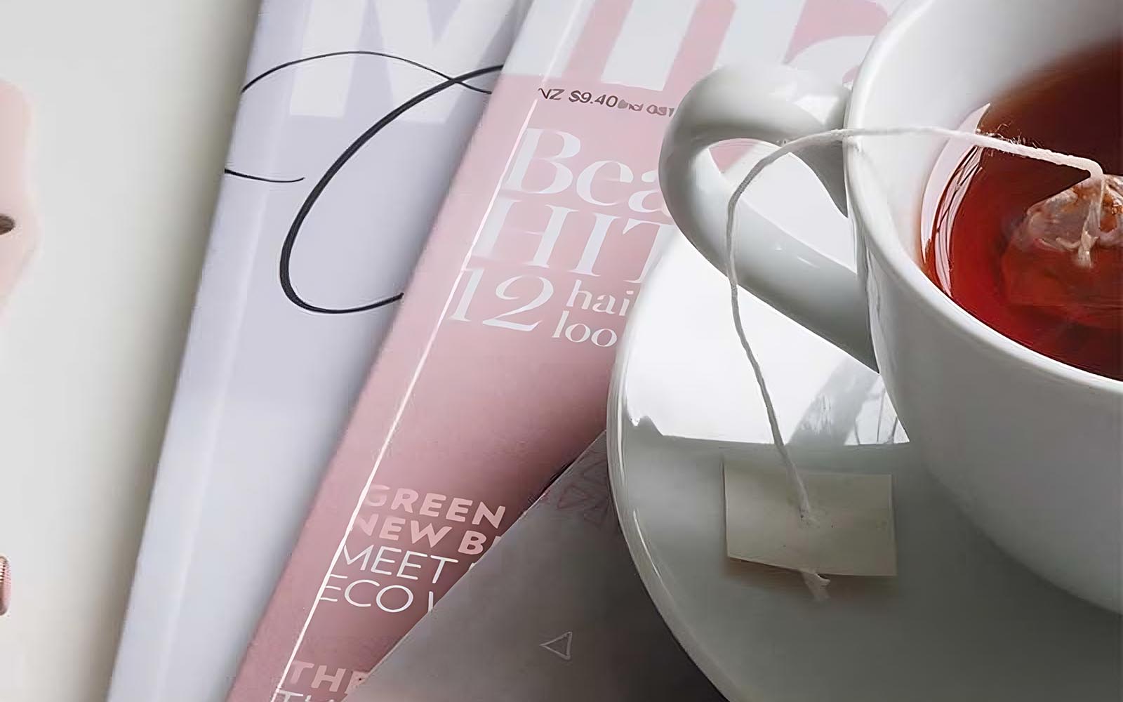 Eine Tasse Tee mit Untertasse und Teebeutel und darunter liegen 3 Magazine